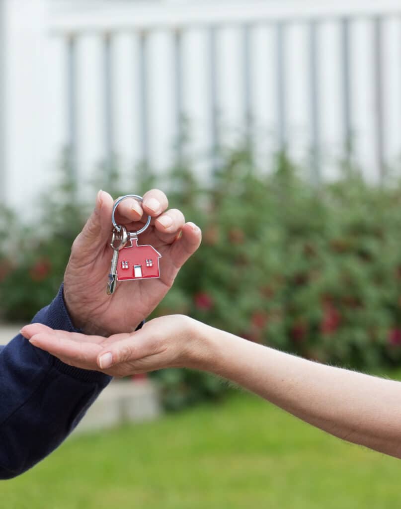 Remise de clés de maison avec porte-clés rouge en forme de maison entre deux mains, symbolisant l'achat ou la vente.